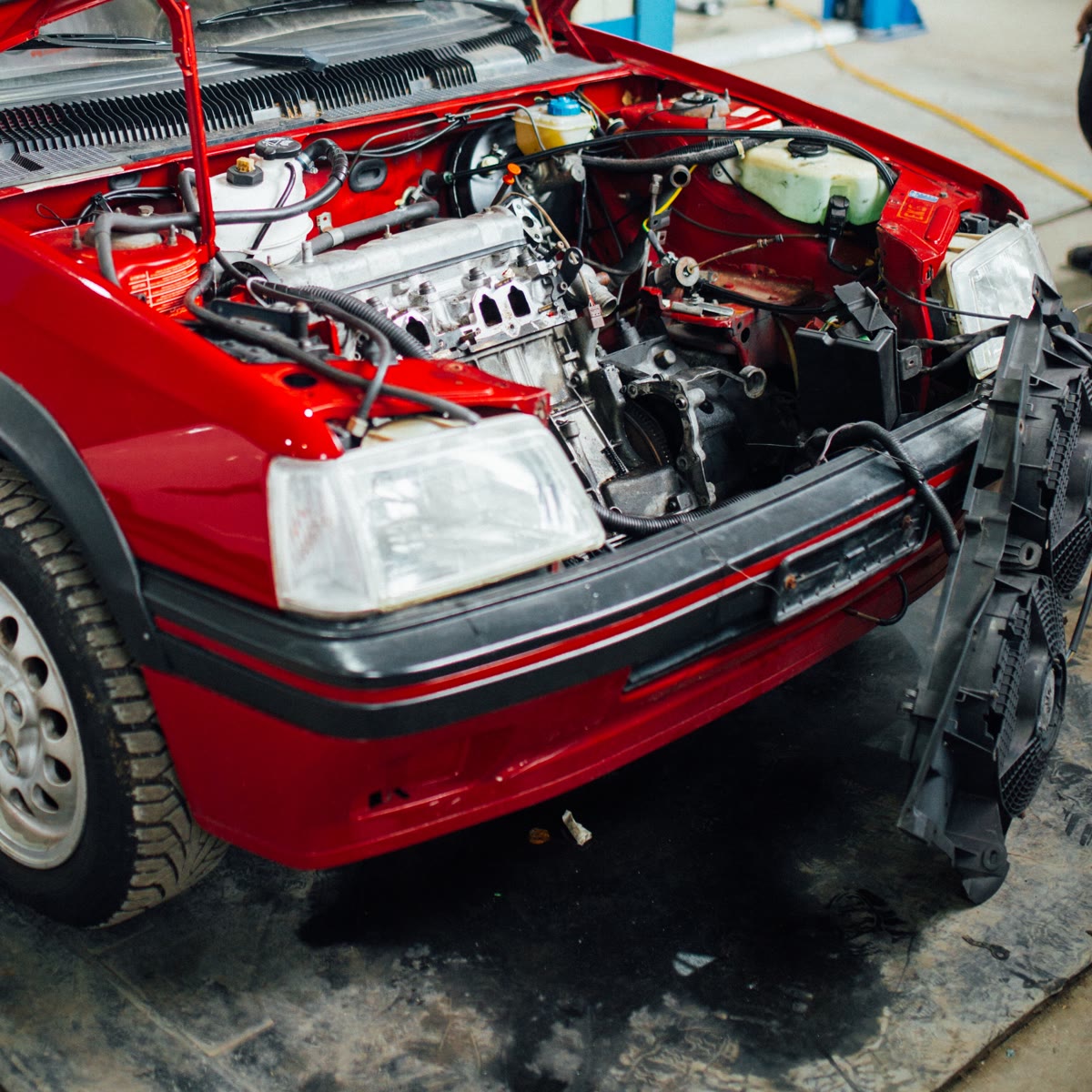 Carro vermelho de capô aberto numa oficina, com o motor e os fios à mostra