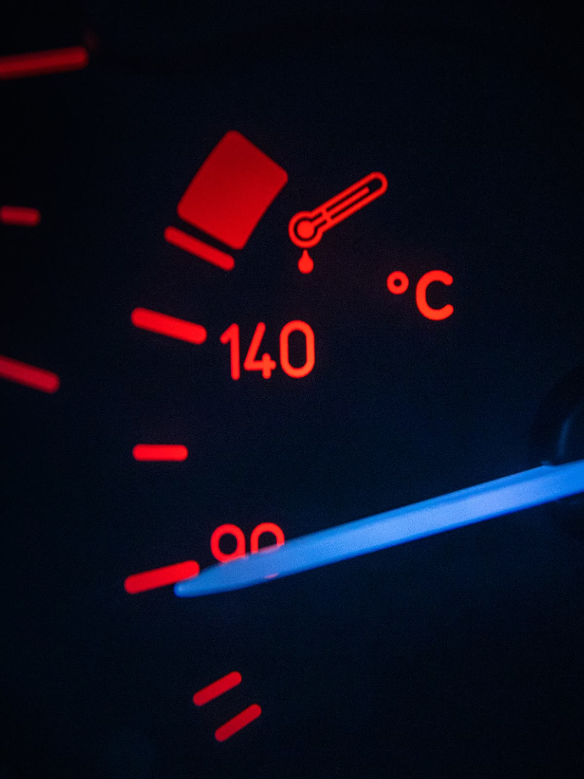Marcador de temperatura do painel de um carro aceso à noite, com os números em vermelho